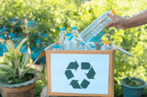 Recycling bin wit plastic bottles inside and someone's hand reaching to put a bottle inside. 